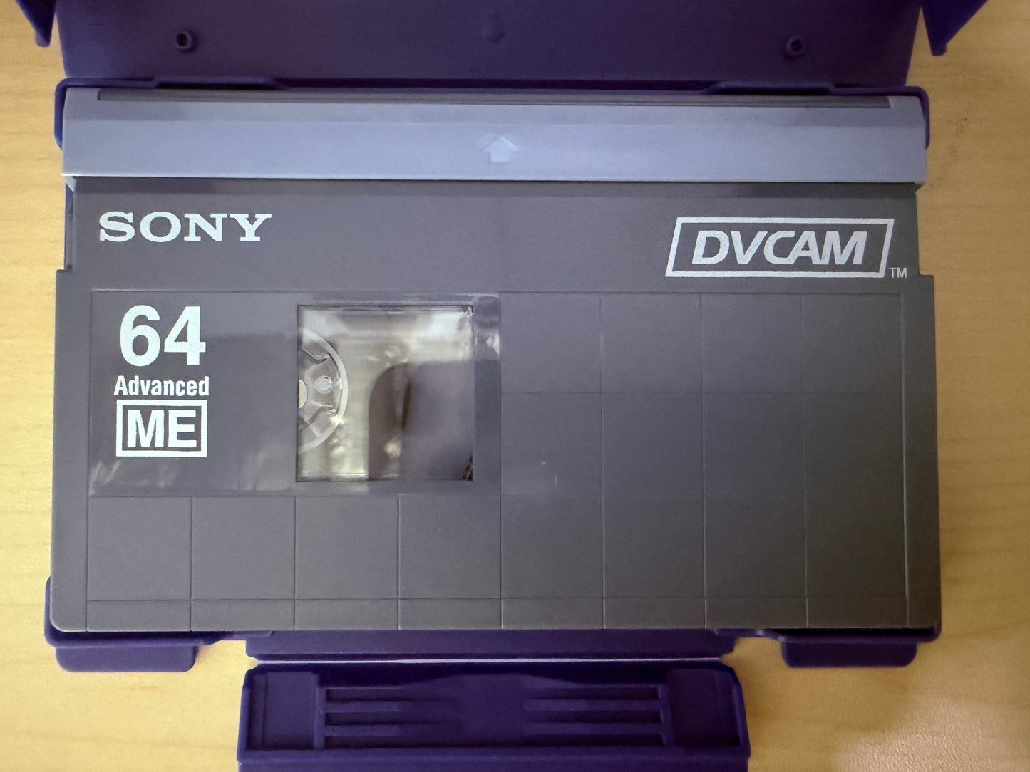 Sony DVCAM tape with '64 Advanced ME' label on a wooden surface