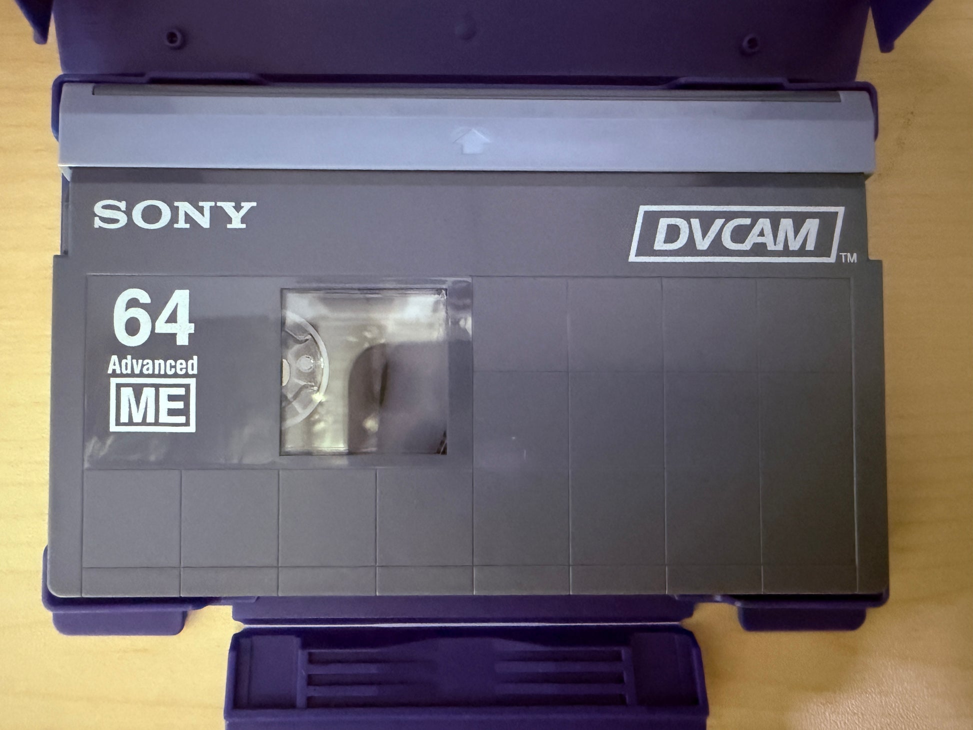 Sony DVCAM tape with '64 Advanced ME' label on a wooden surface